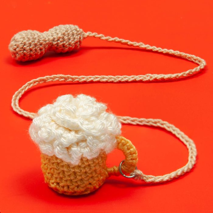 Crochet Handmade Beer Glass With Crochet Peanut Tassel Over The Red Surface Shot